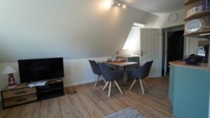 A room with a TV, a dining table with chairs, a lamp, and a clock on the wall. - Ferienwohnung in Wyk-boldixum auf Foehr (Wyk auf Foehr)