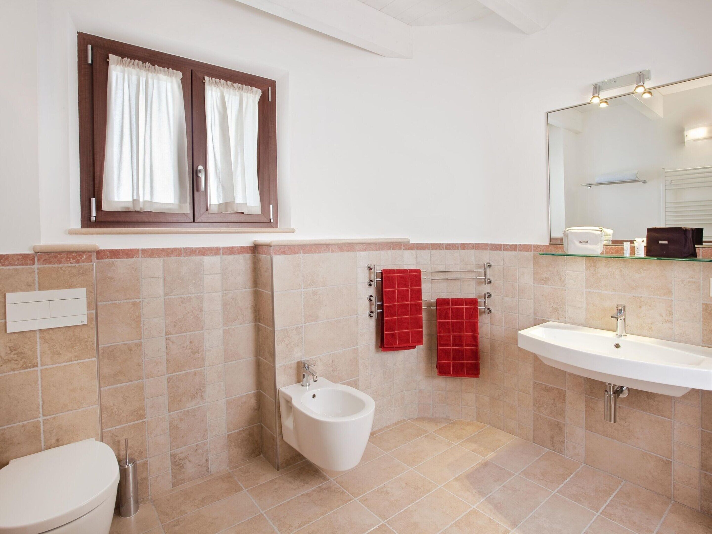 Ein Badezimmer mit Toilette, Bidet, Waschbecken und einem Fenster mit Vorhängen.