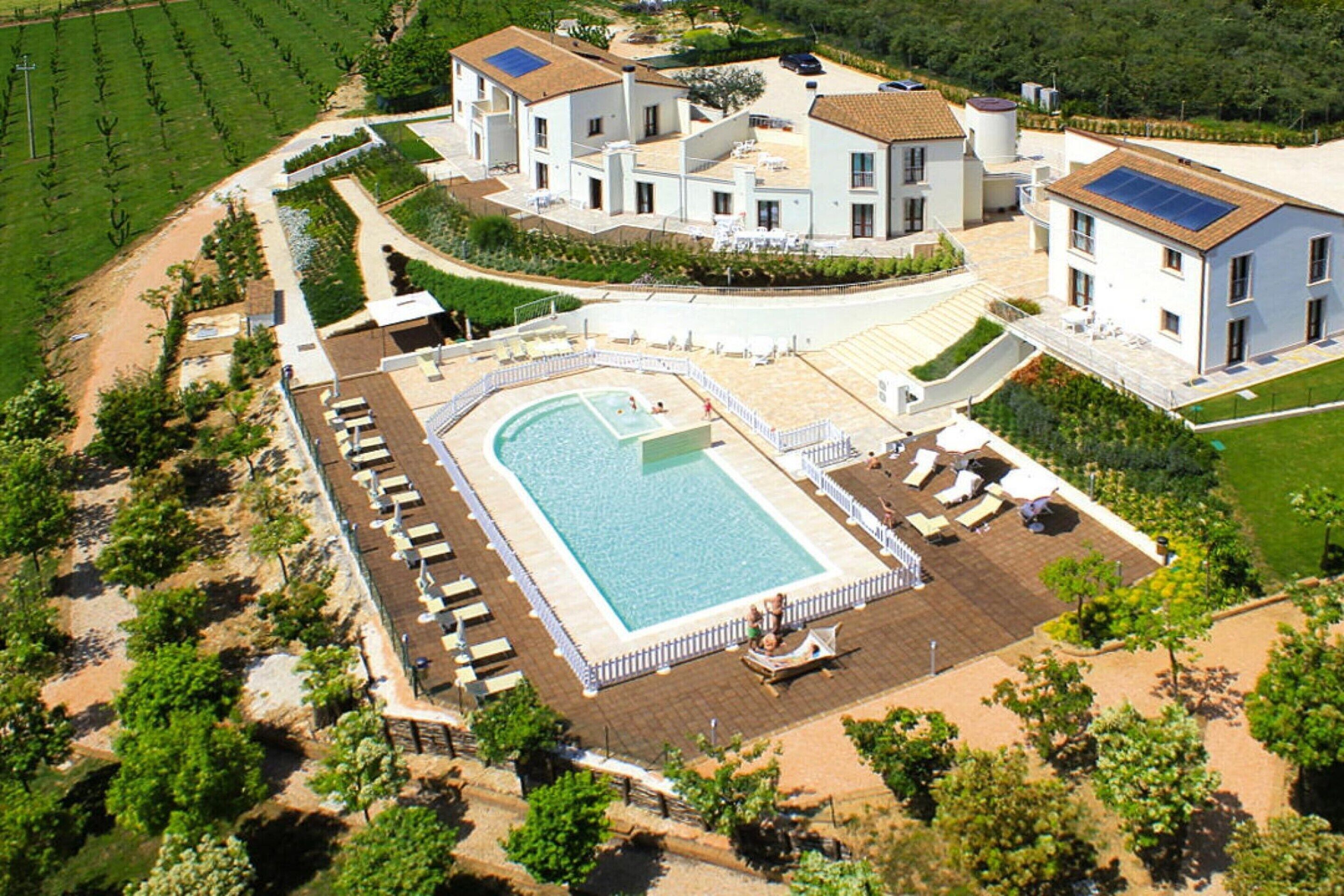 Vue aérienne d’un vaste domaine comprenant une piscine, plusieurs bâtiments et des jardins aménagés.