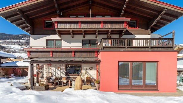 A multi-story building with a red and white facade, balconies, and a covered outdoor seating area. - Apartment in Bramberg Near Wildkogel Arena (Bramberg am Wildkogel)
