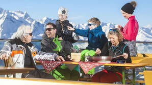 A group of people dining at a table with a mountain view in the background. - Apartment in Bramberg Near Wildkogel Arena (Bramberg am Wildkogel)