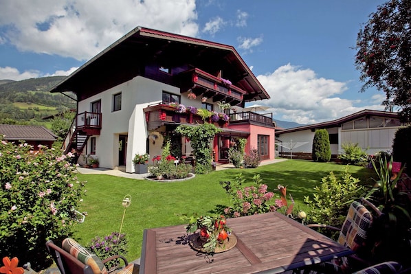 A two-story chalet with a balcony, a well-maintained lawn, and outdoor seating.
