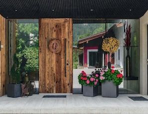 A wooden door with a circular decoration, a glass entrance, and potted plants with flowers.