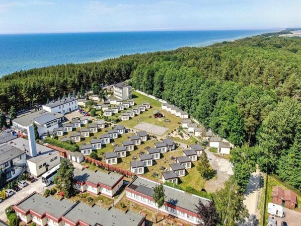 A coastal residential area with multiple small houses, a large building, and a forested hill. - Holiday Home in Lazy by Seaside Beach (gmina Sianów)
