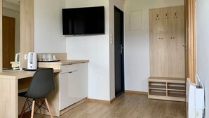 A modern hotel room with a flat-screen TV mounted on the wall, a wooden desk with a chair, a small kitchenette, and a wardrobe with a mirror. - Single-story Holiday Homes Close to the Beach (gmina Sianów)