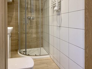 A bathroom with a glass-enclosed shower, a white toilet, and tiled walls. - Holiday Home in Lazy by Seaside Beach (gmina Sianów)