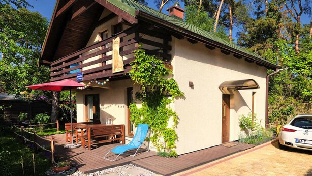 A wooden cabin with a balcony, a red umbrella, and a car parked outside. - Holiday Home in Lukecin Near Baltic Beach (Dziwnów)