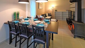 A dining area with a long table set for four, surrounded by chairs, and a modern stove on the right. - Holiday Home in Lukecin Near Baltic Beach (Dziwnów)