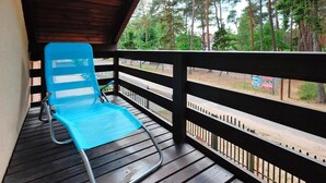 A blue lounge chair on a wooden deck with a metal railing, overlooking a forested area and a road. - Holiday Home in Lukecin Near Baltic Beach (Dziwnów)