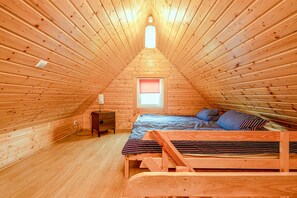 Ein gemütliches Schlafzimmer im Dachgeschoss mit schrägen Wänden, einem Bett mit gestreifter Bettdecke, einem Nachttisch und einem Fenster mit rotem Rollo.