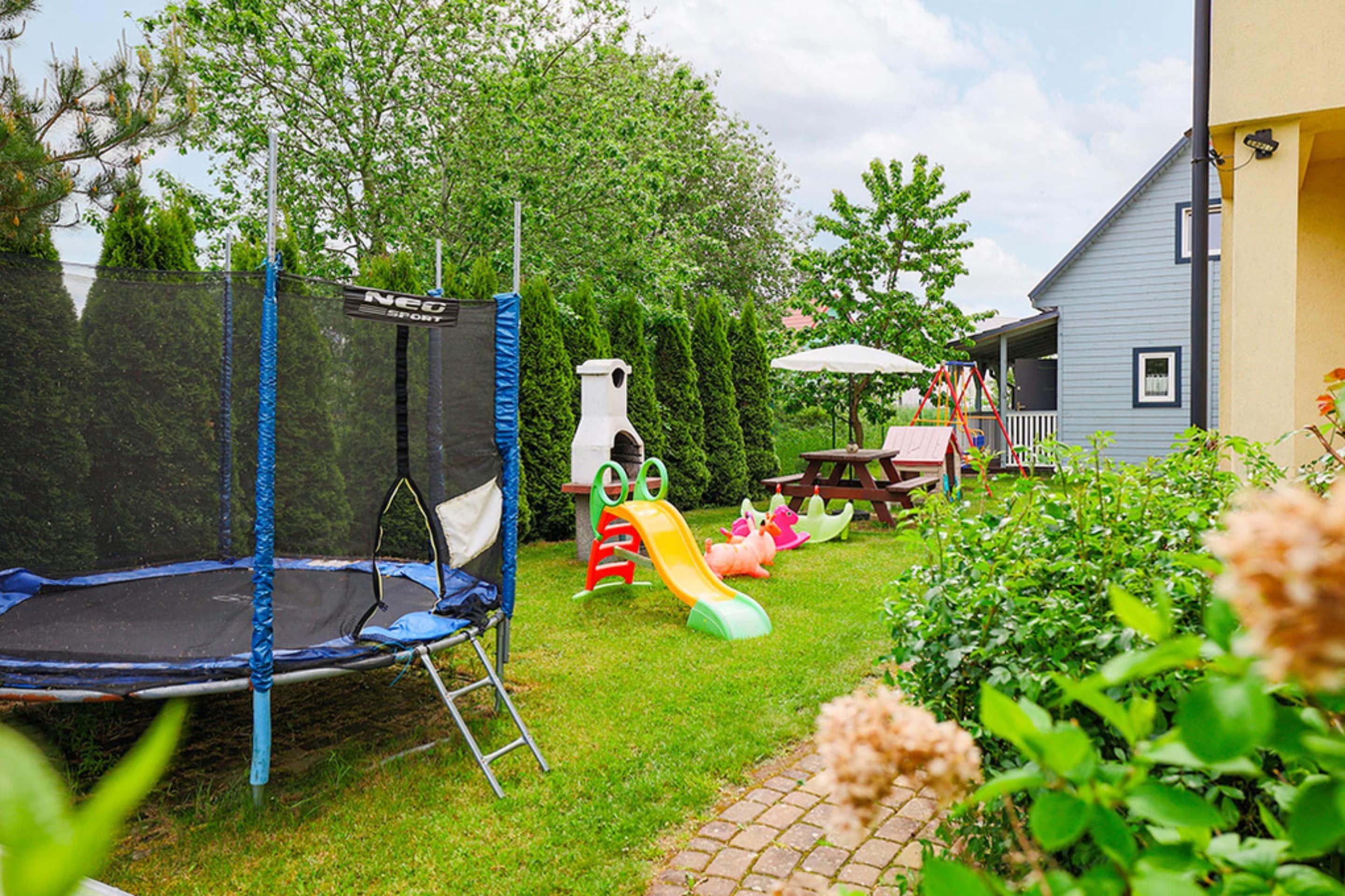Patio trasero con un trampolín, estructuras de juego y una mesa de picnic.