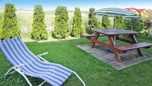A picnic table with a striped umbrella, a striped lounge chair, and a well-maintained lawn with trimmed hedges in the background. - Chalet in Rewal Near Baltic Sea Beach (Rewal)
