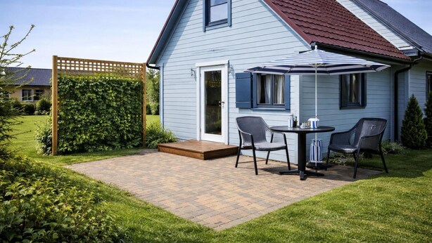 A house with a blue exterior, a red roof, a wooden fence, and a patio with a table and chairs. - Chalet in Rewal Near Baltic Sea Beach (Rewal)