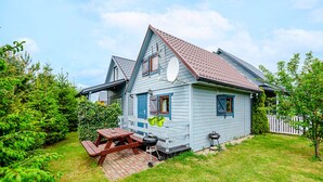 A two-story house with a blue exterior, a red roof, and a satellite dish. There is a wooden deck with a picnic table and a grill.