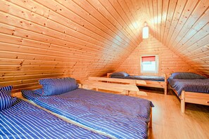 A cozy attic bedroom with wooden walls and sloped ceilings, featuring two beds with striped bedding and a small window. - Chalet in Rewal Near Baltic Sea Beach (Rewal)