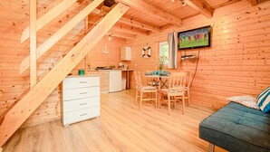 A wooden cabin interior with a dining area, kitchen, and a staircase.