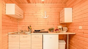 A compact kitchen with wooden walls, a built-in sink, a stove, and a small refrigerator.