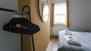 Una camera d'albergo con un letto, uno specchio, un appendiabiti con grucce e una finestra con tende.