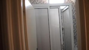 Eine weiße, geschlossene Tür mit Griff, eine geflieste Wand und ein Fenster darüber.