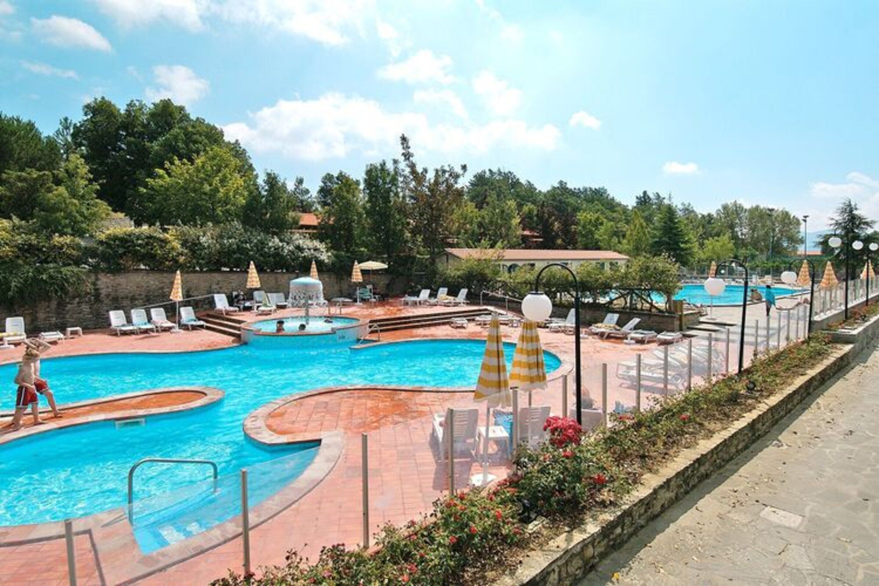 A swimming pool area with multiple pools, sun loungers, and umbrellas.