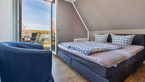A bedroom with a bed, a chair, and a view through a glass door to an outdoor area. - Apartment on Lake Muritz With Marina Access (Buchholz)