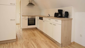 Una cocina moderna con armarios blancos, horno empotrado, lavavajillas y encimera de madera.
