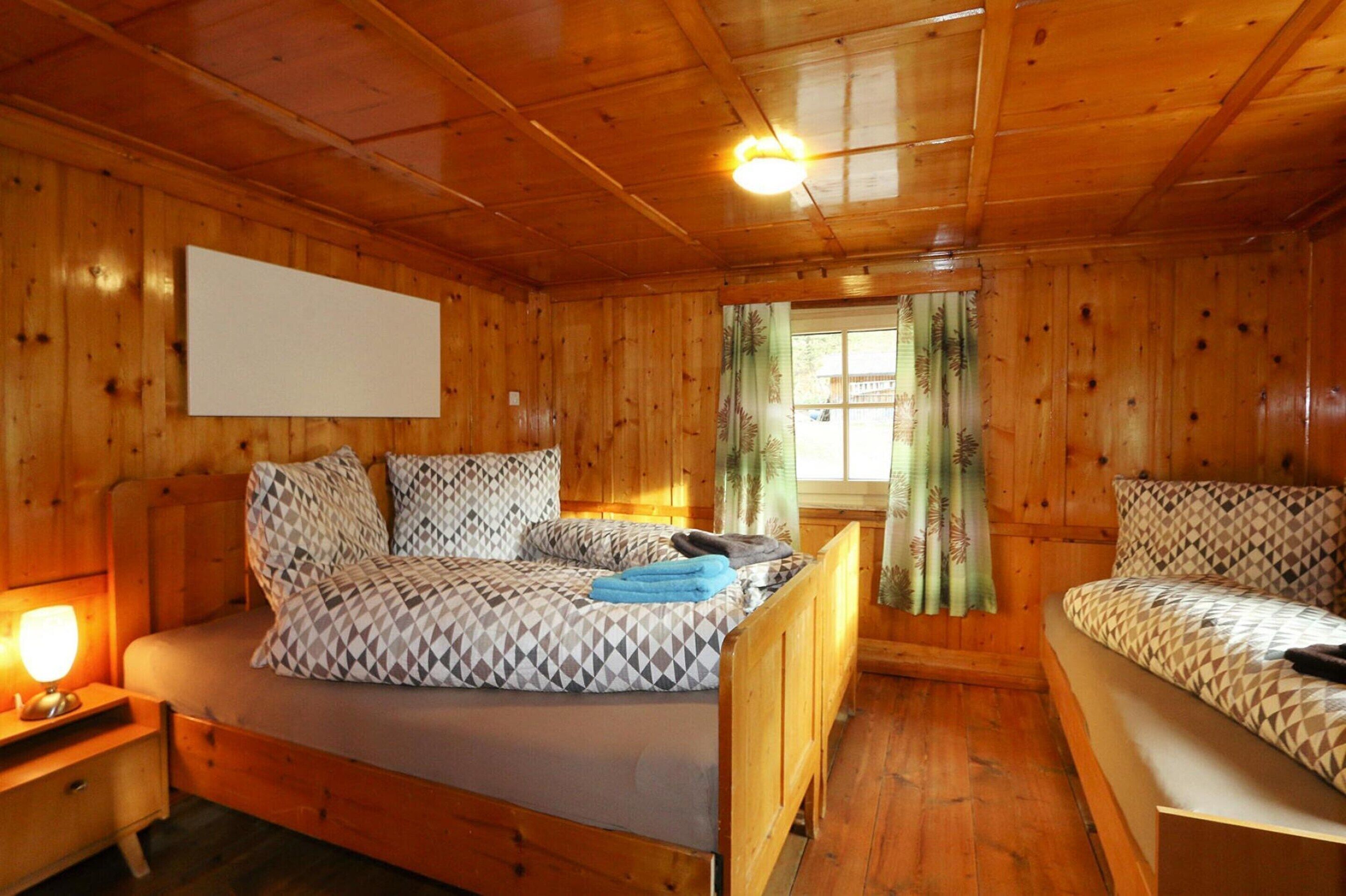 Een houten kamer met een bed, een nachtkastje en een raam met gordijnen.
