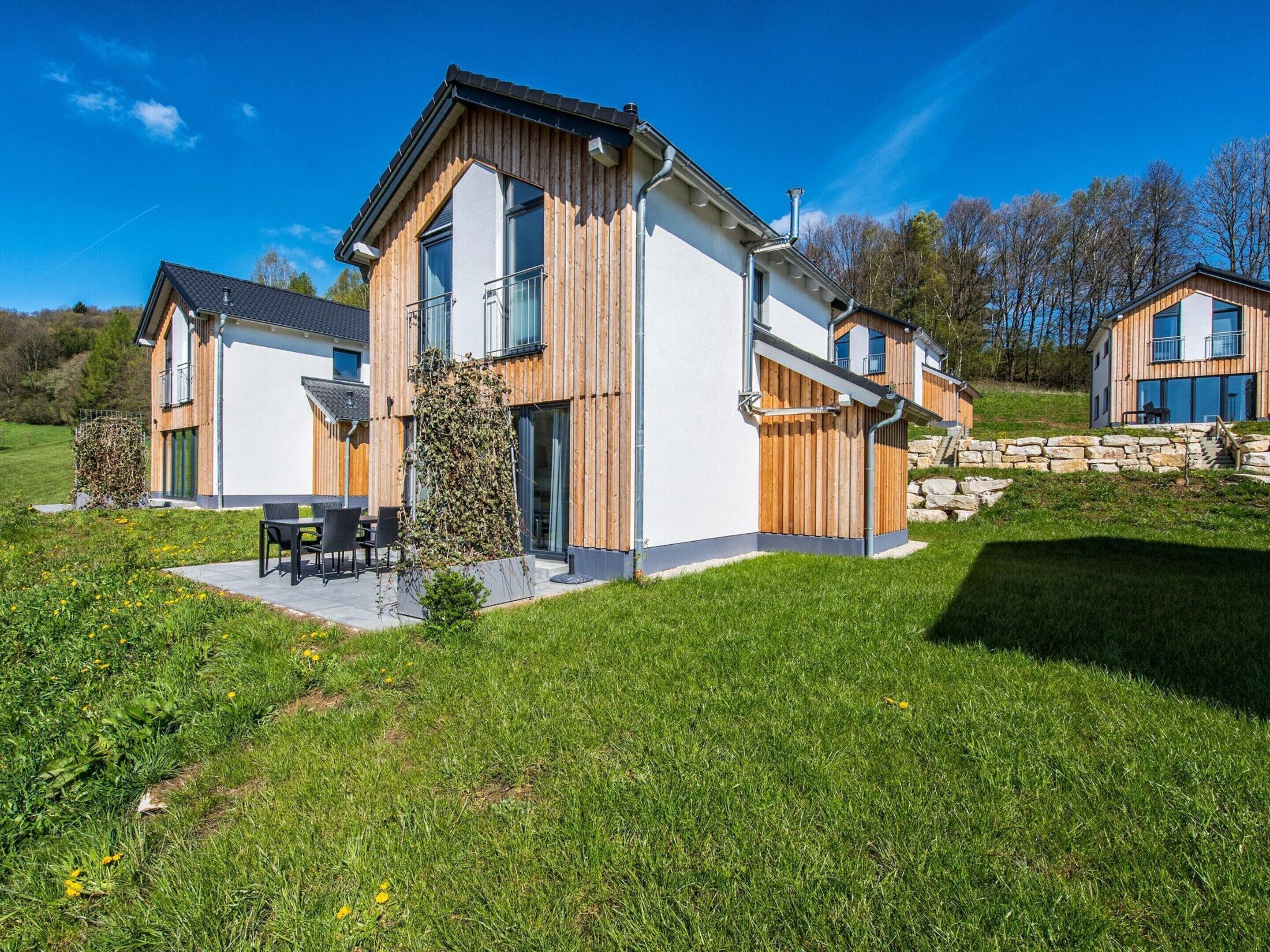 Une maison moderne à deux étages, dotée d’un grand patio, d’un escalier en pierre et offrant une vue sur le paysage environnant.
