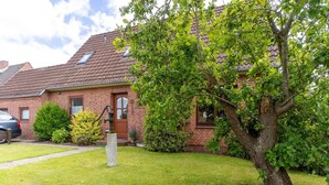 A brick house with a tiled roof, a well-maintained lawn, and a large tree in the front yard.