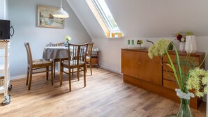 A dining area with a table and chairs, a wooden cabinet, and a vase with flowers.