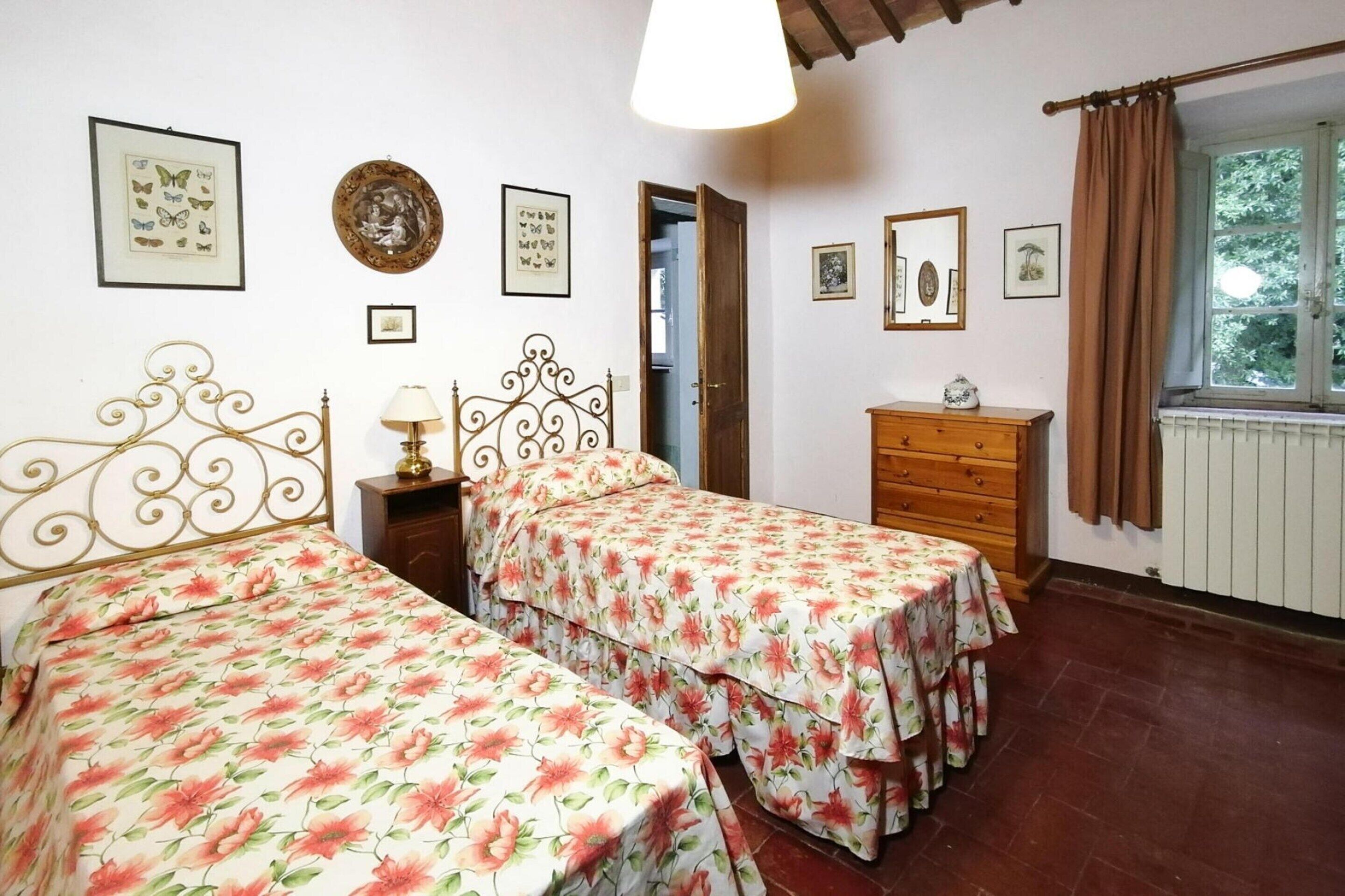 A bedroom with two beds, a wooden dresser, and a window with curtains.