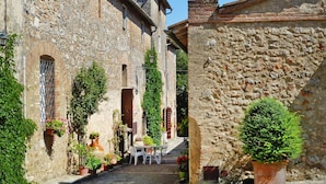 Un vicolo stretto con edifici in pietra, piante in vaso e un tavolo con sedie.