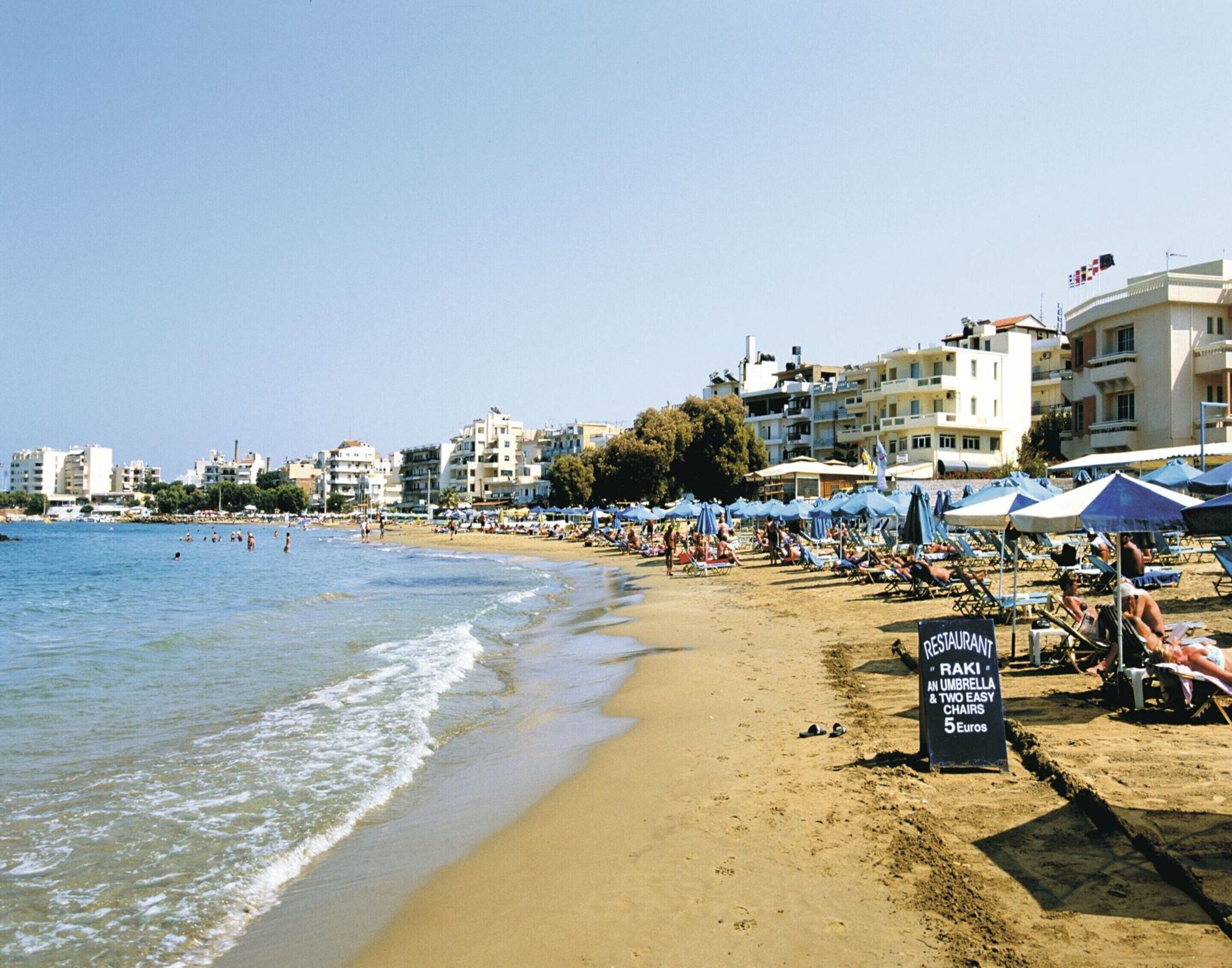 A beach with umbrellas, a sign for a restaurant, and buildings in the background.