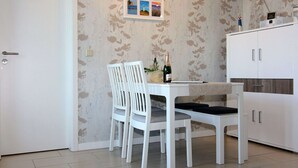Un comedor con una mesa blanca, dos sillas blancas, una botella de champán y un cuadro en la pared.