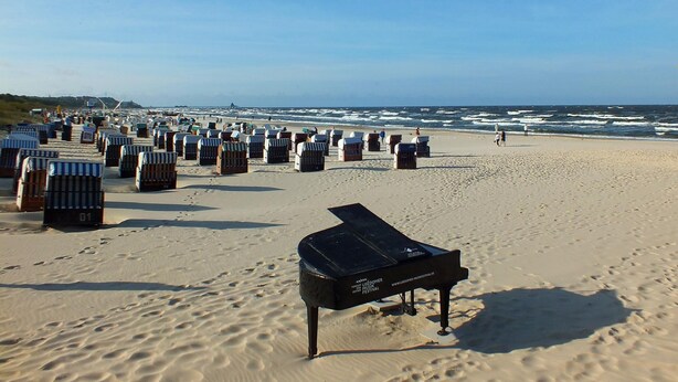 Una playa con hileras de sillas de playa a rayas y un piano negro al frente.