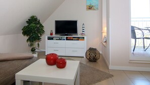 Un salón con un televisor de pantalla plana, una planta y dos manzanas rojas sobre una mesa.