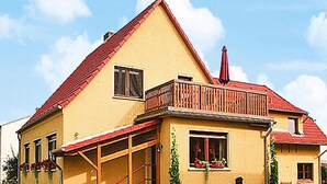 Una casa de dos pisos con techo rojo, un balcón y un porche cubierto.