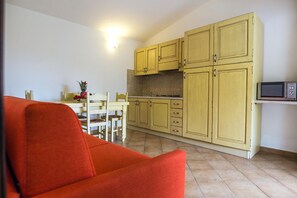 A compact kitchen with yellow cabinets, a microwave, and a dining area with a red chair. - Flat With Communal Pool in the Residence Badus in Badus-formerly TUI Ferienhaus (Badesi)