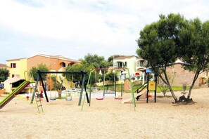 Un terrain de jeux avec des balançoires et des toboggans, entouré d’immeubles d’habitation.
