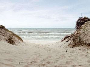 Ein sandiger Strand mit Dünen und dem Meer im Hintergrund.
