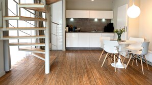 Une cuisine moderne avec des meubles blancs, un coin repas avec des chaises blanches et un escalier en bois.