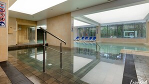 Un espace piscine intérieure doté d’une paroi en verre, de chaises longues bleues et offrant une vue dégagée sur l’extérieur.