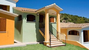 Una casa de dos pisos con una escalera que lleva al nivel superior, un porche delantero y un pequeño jardín.