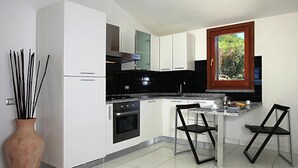 Cocina moderna con armarios blancos, encimera negra y horno integrado. Se ve una ventana con vistas a árboles y, a la izquierda, un florero con ramas.