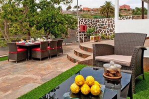 An outdoor patio with wicker furniture, a glass table with lemons, and a stone wall with a red box. - Dream Villa With Pool in Ingenio (Ingenio)