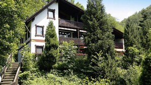 A two-story chalet with a balcony, surrounded by dense forest and a wooden staircase leading to the entrance. - Ferienwohnung im Haus Schiefertal, Wieda (Walkenried)