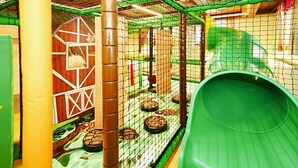 An indoor play area with a green slide, netted play structures, and a barn-themed playhouse. - Apartment In Flachau With Balcony (Flachau)