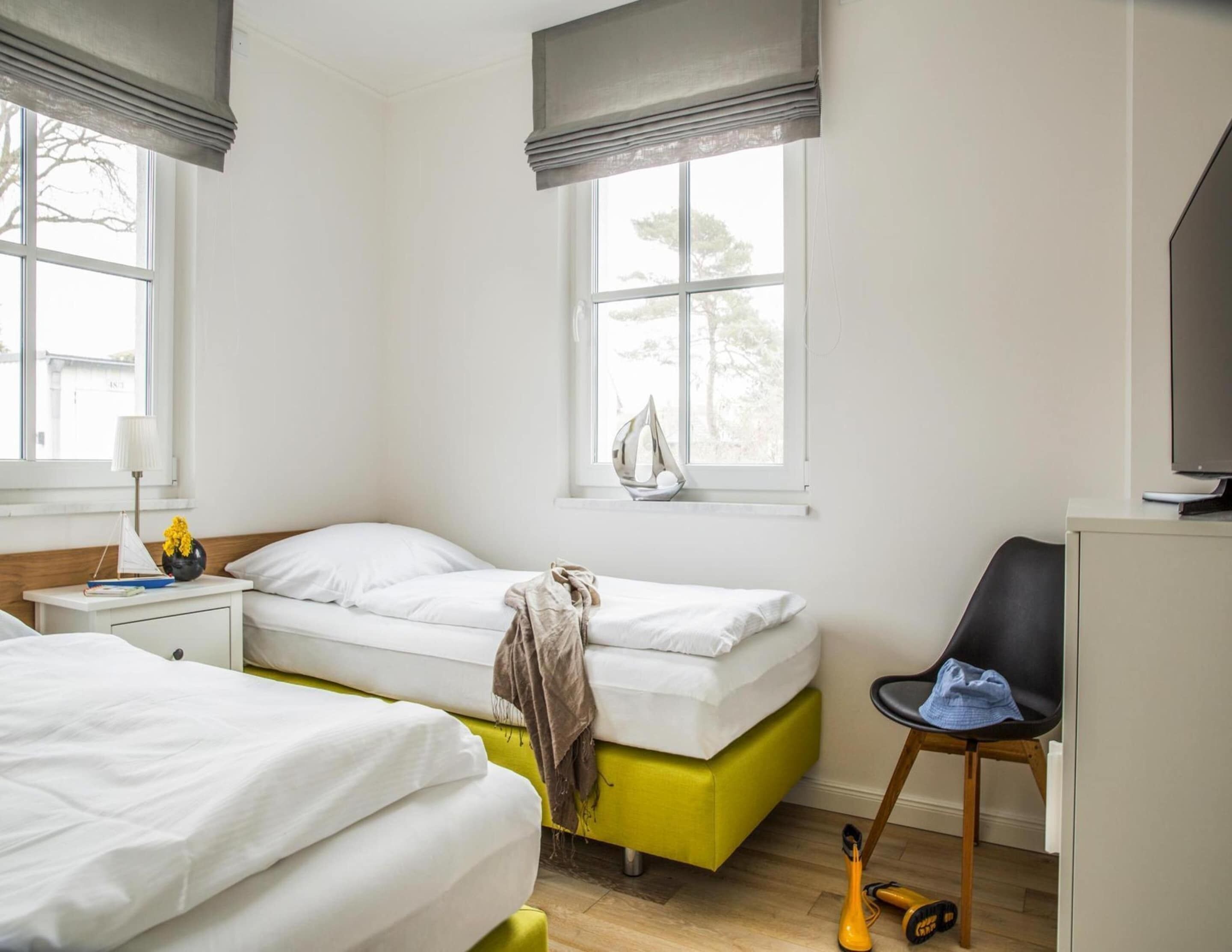 A bedroom with two beds, a chair, a desk, and a window with a view.