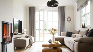Ett modernt vardagsrum med en soffa, ett soffbord, en tv och ett stort fönster med gardiner.