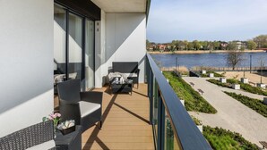 A balcony with wicker furniture and a view of a lake and buildings. - Premium Apartment With Pool and Sauna (Dziwnów)